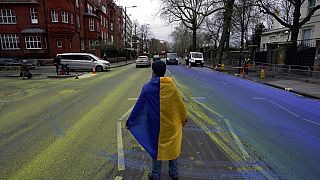 A protester wears a Ukraine flag after a group of activist artists painted a giant Ukrainian flag outside the Russian Embassy in London, Thursday, Feb. 23, 2023.