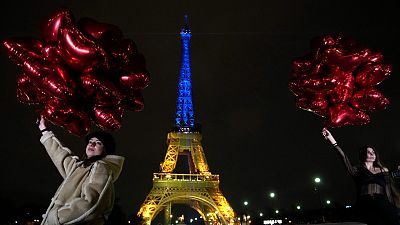 Tourists pose with balloons as the Eiffel Tower is lit up in Ukraine's colours to mark the one-year anniversary of Russia's invasion, Paris, February 23, 2023.