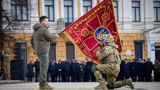 ولودیمیر زلنسکی، رئیس جمهوری اوکراین در مراسم نخستین سالگرد آغاز تهاجم نظامی روسیه به اوکراین در کی‌یف پرچم یک واحد نظامی را در دست دارد و سربازی آن را می‌بوسد