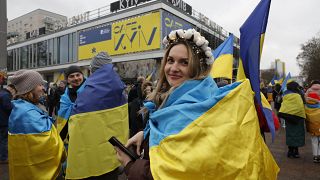 Demonstrators wrapped into flags of Ukraine stand in front of Berlin's Cafe Moskau (Cafe Moscow) that has been renamed to Cafe Kyiv for several days, on February 24, 2023