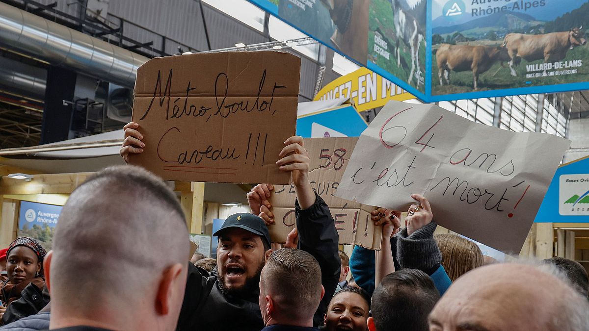 فرنسيون يحملون لافتات كتب عليها "مترو، عمل، قبر" أثناء احتجاجهم ضد رفع الحد الأدنى لسن التقاعد خلال زيارة ماكرون لمعرض باريس للفلاحة. 2023/02/25