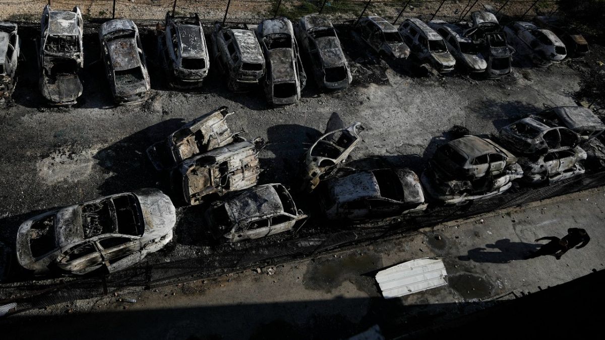 Palestinians walk past burned cars in the town of Hawara, near the West Bank city of Nablus, Monday, Feb. 27, 2023.