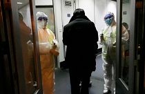 Health Officials in hazmat suits wait at the gate to check body temperatures of passengers arriving from the city of Wuhan, at the airport in Beijing, China, Jan. 22, 2020.