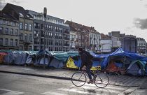 A man rides his bike past a makeshift tent camp outside the Petit Chateau reception centre in Brussels, Tuesday, Jan. 17, 2023