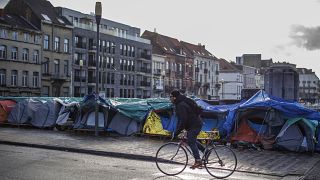 A man rides his bike past a makeshift tent camp outside the Petit Chateau reception centre in Brussels, Tuesday, Jan. 17, 2023