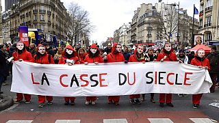 Manifestantes com máscaras do presidente francês Emmanuel Macron seguram faixa onde se lê "O roubo do século", esta terça-feira, em Paris