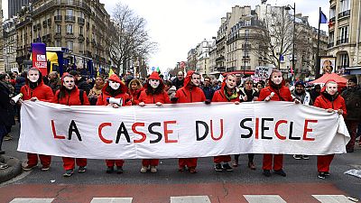 Manifestantes com máscaras do presidente francês Emmanuel Macron seguram faixa onde se lê "O roubo do século", esta terça-feira, em Paris