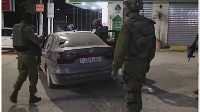 قوات الدفاع الإسرائيلية وهي تتفقد السيارة المتضررة بعد هجوم مستوطنين على محلات تجارية وسيارات في بلدة حوارة في الضفة الغربية، 6 مارس/ آذار 2023.