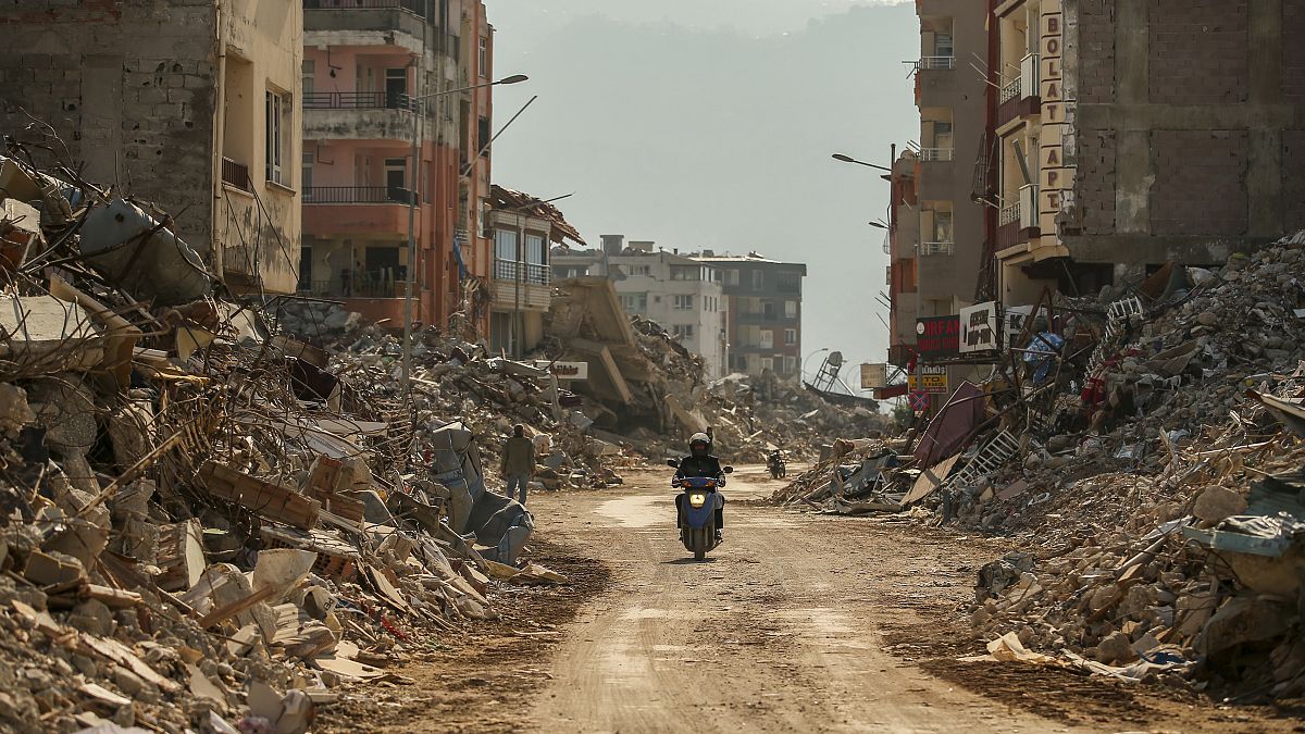 رجل على متن دراجة نارية بالقرب من حطام المباني المدمرة في سامانداج، في جنوب تركيا 