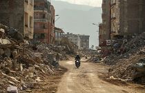 رجل على متن دراجة نارية بالقرب من حطام المباني المدمرة في سامانداج، في جنوب تركيا