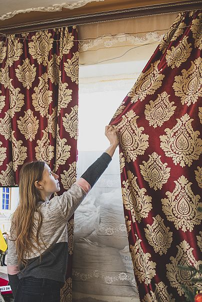 Alina closes the curtains to cover the windows which are reinforced by bags for safety during shelling, it's "cosier" this way, she says.
