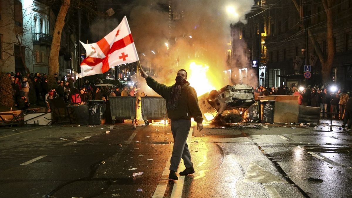 FILE -  man waves a Georgian national flag in front of a burning barricade as other protesters stand behind near the Georgian parliament building in Tbilisi, 9 March 2023.