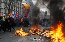 Protesters walk past a burning pallets during a demonstration in Paris, Saturday, March 11, 2023. 