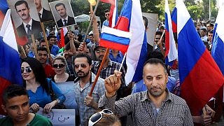 Ciudadanos sirios sujetan fotos del presidente Assad y banderas de Rusia en una protesta en agradecimiento por la intervención rusa en Siria.