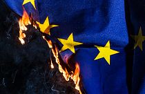 An EU flag burns. 