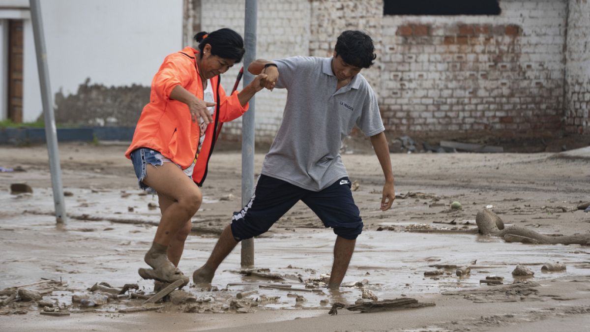 Pessoas caminham na lama resultado da chuva provocada pelo ciclone Yaku