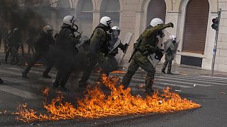 Riot police officers walk among flames of petrol bombs thrown by protestors during a protest in central Athens, Thursday, March 16, 2023. 