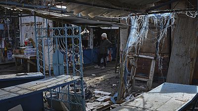 A vendor waits for customers at a local market with partially damaged shops after shelling attacks in the town of Orekhovo, Ukraine, Wednesday, March 15, 2023