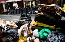A man (top) walks past a pile of garbage bags that have been piling up since waste collectors went on strike. 15 March 2023