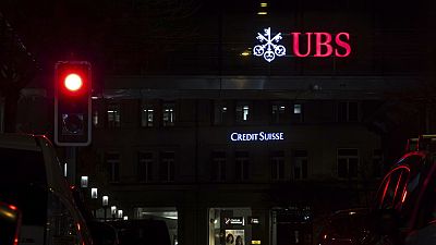 The illuminated logos of the Swiss banks Credit Suisse and UBS are seen on buildings next to traffic lights in Zurich, Switzerland