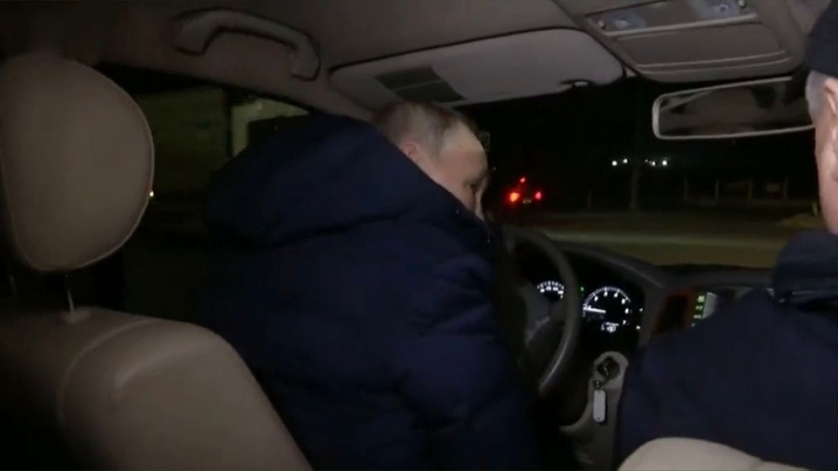 Vladimir Putin, di spalle, al volante di un'automobile per le strade di Mariupol.
