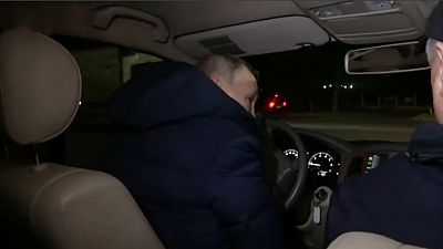Vladimir Putin, di spalle, al volante di un'automobile per le strade di Mariupol.