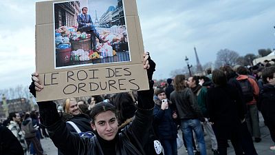 A woman holds a placard depicting French President Emmanuel Macron sitting on garbage cans that reads, "king of trash" during a protest in Paris, Friday, March 17, 2023. 