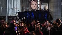 Protesters hold a banner with Emmanuel Macron's face during a protest in Paris, Saturday, March 18, 2023.