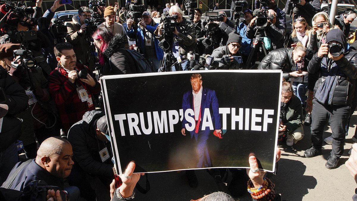 Una mujer sostiene un cartel como parte de una protesta frente al tribunal antes de la acusación anticipada del expresidente Donald Trump, 20 de marzo de 2023, Nueva York