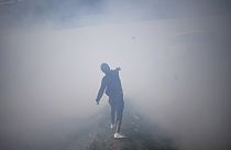 A protester covered in tear gas throws a rock at French police officers as he and oil workers block the access to an oil depot in Fos-sur-Mer, France, March, 21, 2023. 