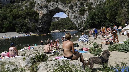 People relax on a beach next to "Le Pont d'Arc" rock on the Ardeche river in the Gorges de l'Ardeche.
