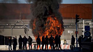 کارگران بارانداز در مقابل یک سنگر در حال سوختن در بندر مارسی در جنوب فرانسه ایستاده‌اند