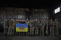 Volodymyr Zelensky aux côtés de soldats ukrainiens tient le drapeau d'une unité militaire près de Bakhmut, en Ukraine, 22/03/2023