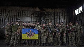 Volodymyr Zelensky aux côtés de soldats ukrainiens tient le drapeau d'une unité militaire près de Bakhmut, en Ukraine, 22/03/2023