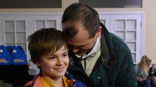 Denys Zaporozhchenko (R) and his ten-year-old son react after the bus delivering him and more than a dozen other children back from Russian-held territory arrived in Kyiv