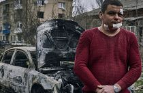 An injured man stands next to the burned car after a Russian attack in Sloviansk, Donetsk region, Ukraine, Monday, March 27, 2023.