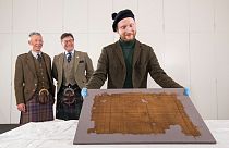 V&A Dundee curator James Wylie with the Glen Affric tartan, with STA's Peter MacDonald and John McLeish looking on