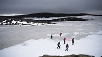 People walk on snow atop the Ok volcano crater on their way to a ceremony by the area which once was the Okjokull glacier