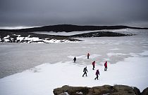 People walk on snow atop the Ok volcano crater on their way to a ceremony by the area which once was the Okjokull glacier