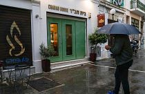 A man holding an umbrella stands in front of a Jewish restaurant that Greek officials believe was one of the targets of a planned terrorist attack, in central Athens, March 28