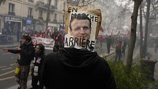 متظاهر يحمل ملصقاً يسخر من الرئيس الفرنسي إيمانويل ماكرون فوق رأسه خلال مظاهرة يوم الثلاثاء 28 مارس 2023 في باريس.
