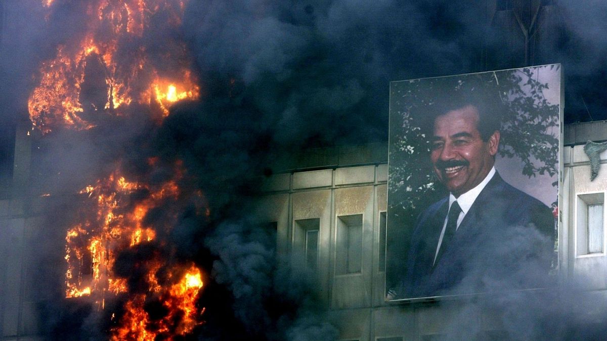 تصویری از صدام حسین بر روی ساختمان آتش زده وزارت حمل و نقل و ارتباطات در بغداد. ۹ آوریل ۲۰۰۳