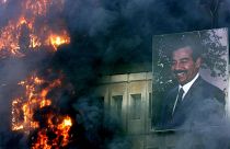 تصویری از صدام حسین بر روی ساختمان آتش زده وزارت حمل و نقل و ارتباطات در بغداد. ۹ آوریل ۲۰۰۳