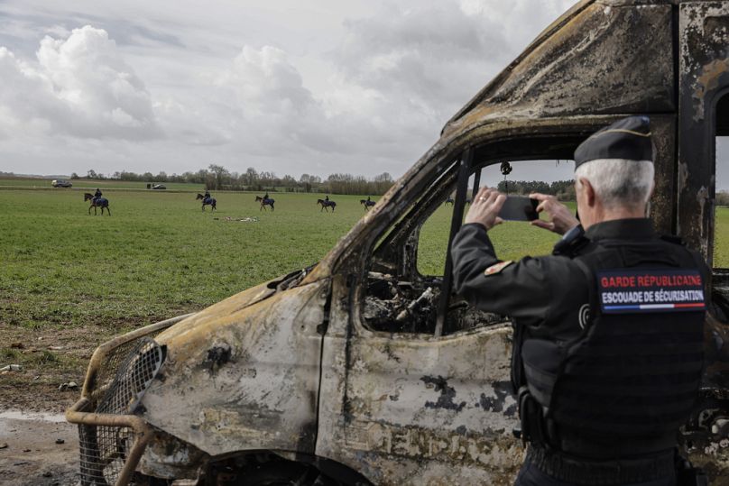 A police officer takes picture with his mobile phone as he stands next burned-out police vehicles after clashes with protesters in Sainte-Soline, western France in March 2023