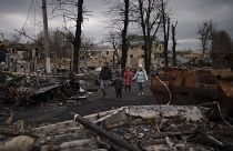 FILE - A family walks amid destroyed Russian tanks in Bucha, on the outskirts of Kyiv, Ukraine, Wednesday, April 6, 2022