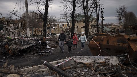 FILE - A family walks amid destroyed Russian tanks in Bucha, on the outskirts of Kyiv, Ukraine, Wednesday, April 6, 2022