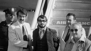 Zvonko Busic, with beard, is led from a plane in custody of police at New York's Kennedy airport after being arrested for air piracy. 12 September 1976 