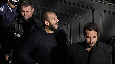 FILE - Police officers escort Andrew Tate handcuffed to his brother Tristan, right, from the Court of Appeal in Bucharest, Romania, on Feb. 1, 2023.