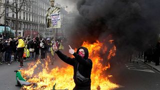 متظاهر يحمل ملصقًا يسخر فيه من الرئيس الفرنسي إيمانويل ماكرون بجوار إحراق صناديق قمامة خلال مظاهرة في باريس. 2023/03/28
