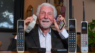 المهندس الأمريكي مارتن كوبر يحمل بيده اليمنى نسخة من أول هاتف محمول استعمله لإجراء أول اتصال قبل نصف قرن